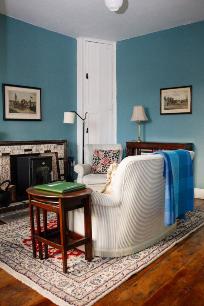 A fireside sitting room with a blue armchair and rug inside Parade House
