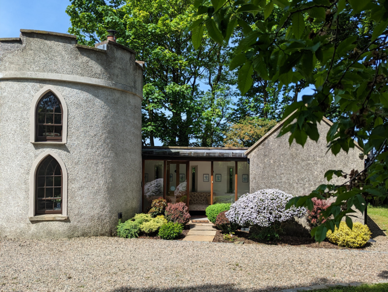A classical gatelodge with round tower, set in woodland.
