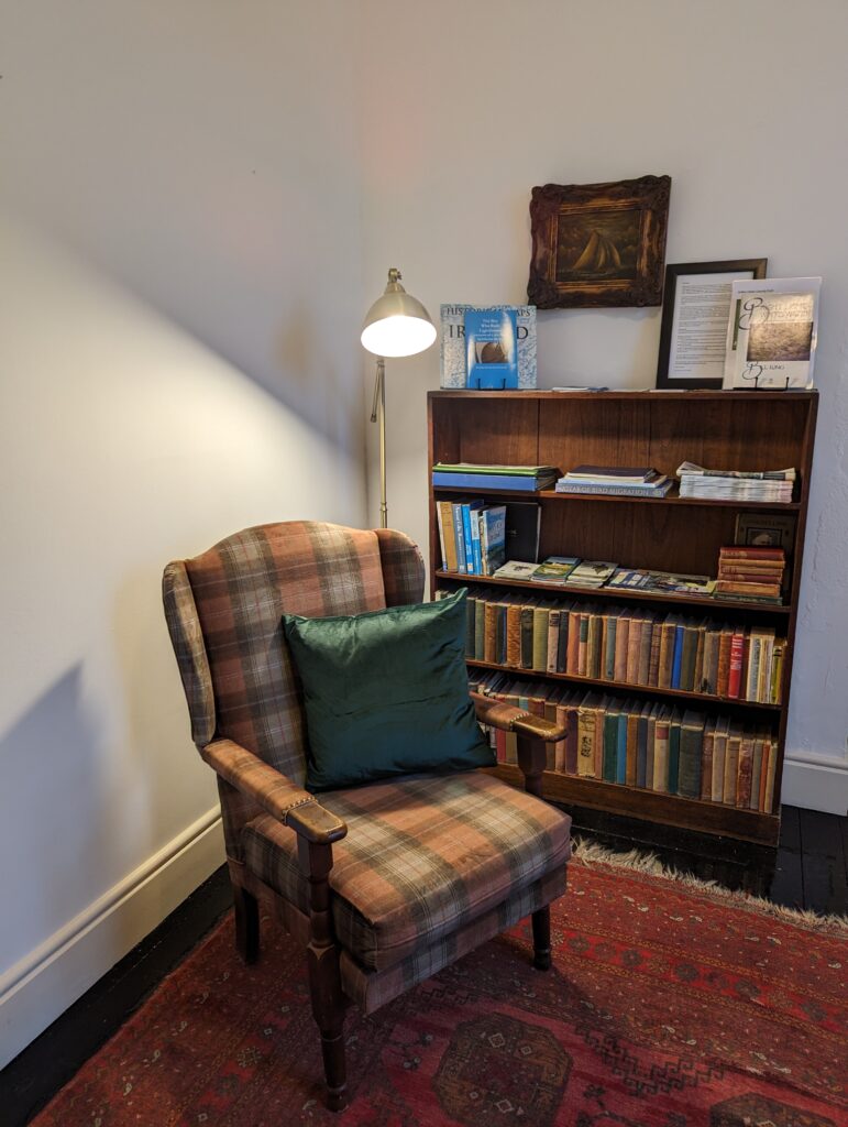 A cosy reading nook with a tartan armchair and a full bookcase at Galley Head
