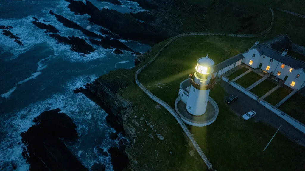 Galley Head Lighthouse and its keepers' houses on a clifftop at night, the beam lit above the waves